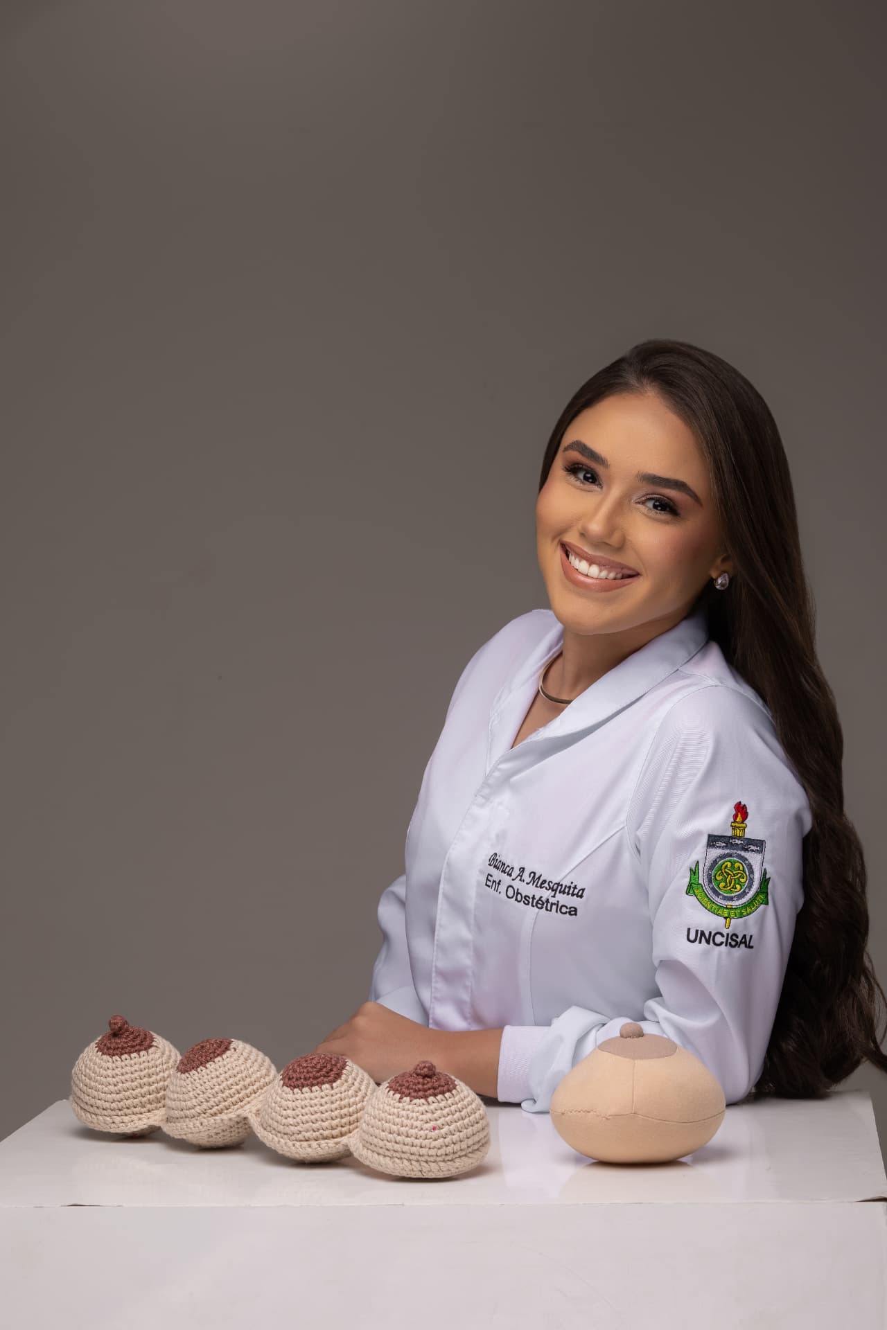 Bianca Almeida sorrindo em estúdio, com modelo didático de amamentação