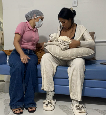 Imagem ilustrativa de profissional de saúde orientando mãe sentada com bebê no colo