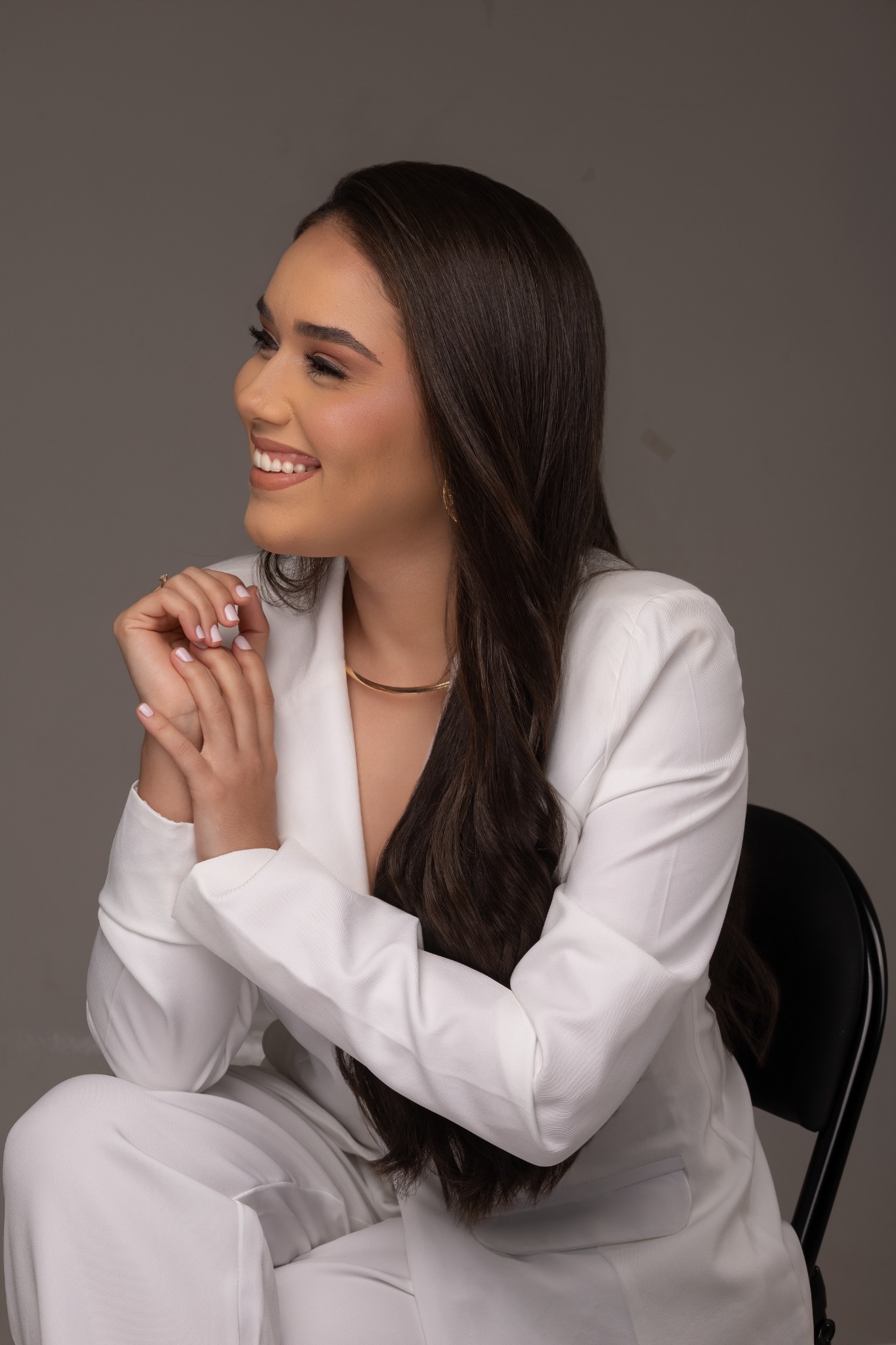 Bianca Almeida sentada, sorrindo, de blazer branco